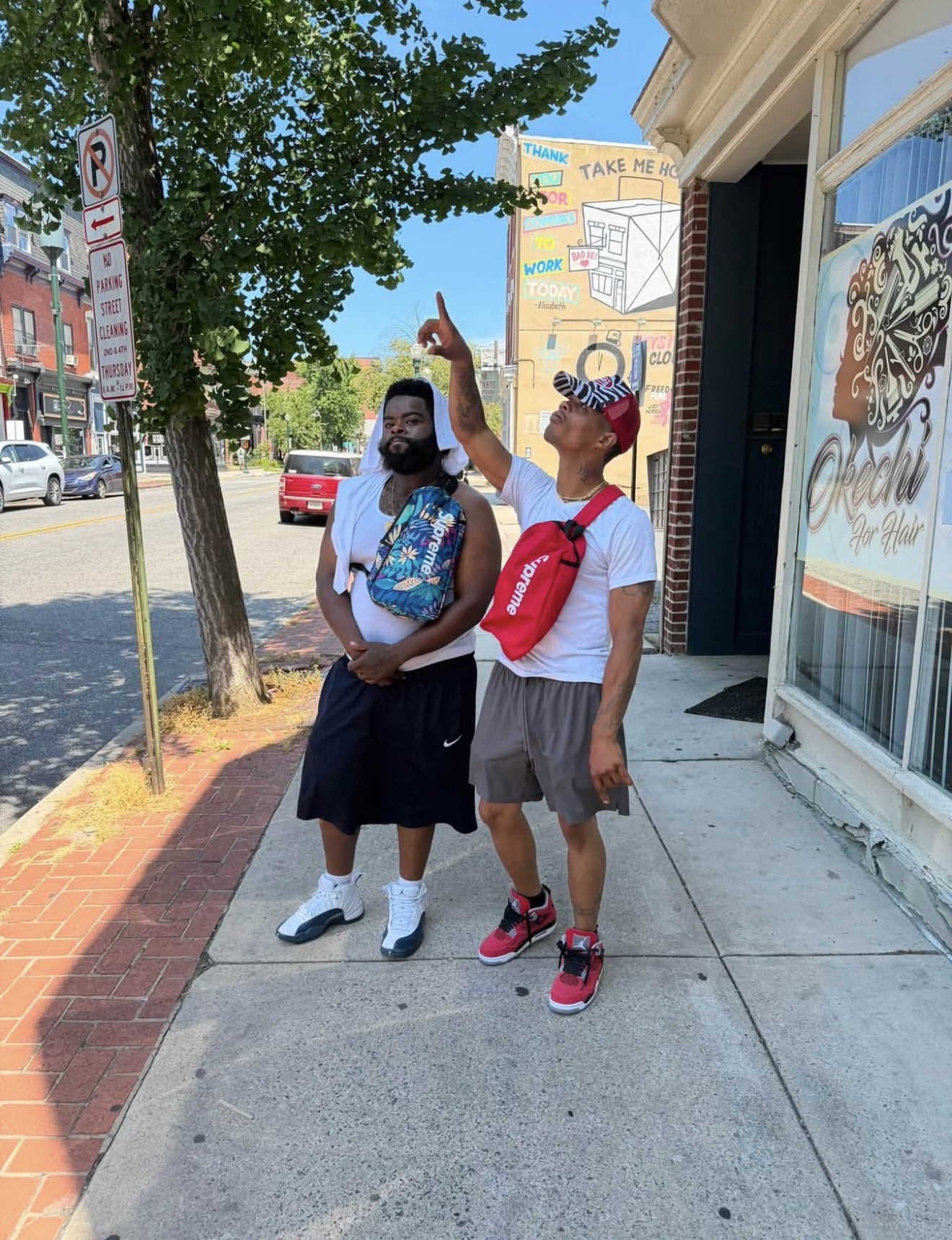 Mr. Supreem pointing skyward on a Harrisburg sidewalk with a friend, both wearing bags